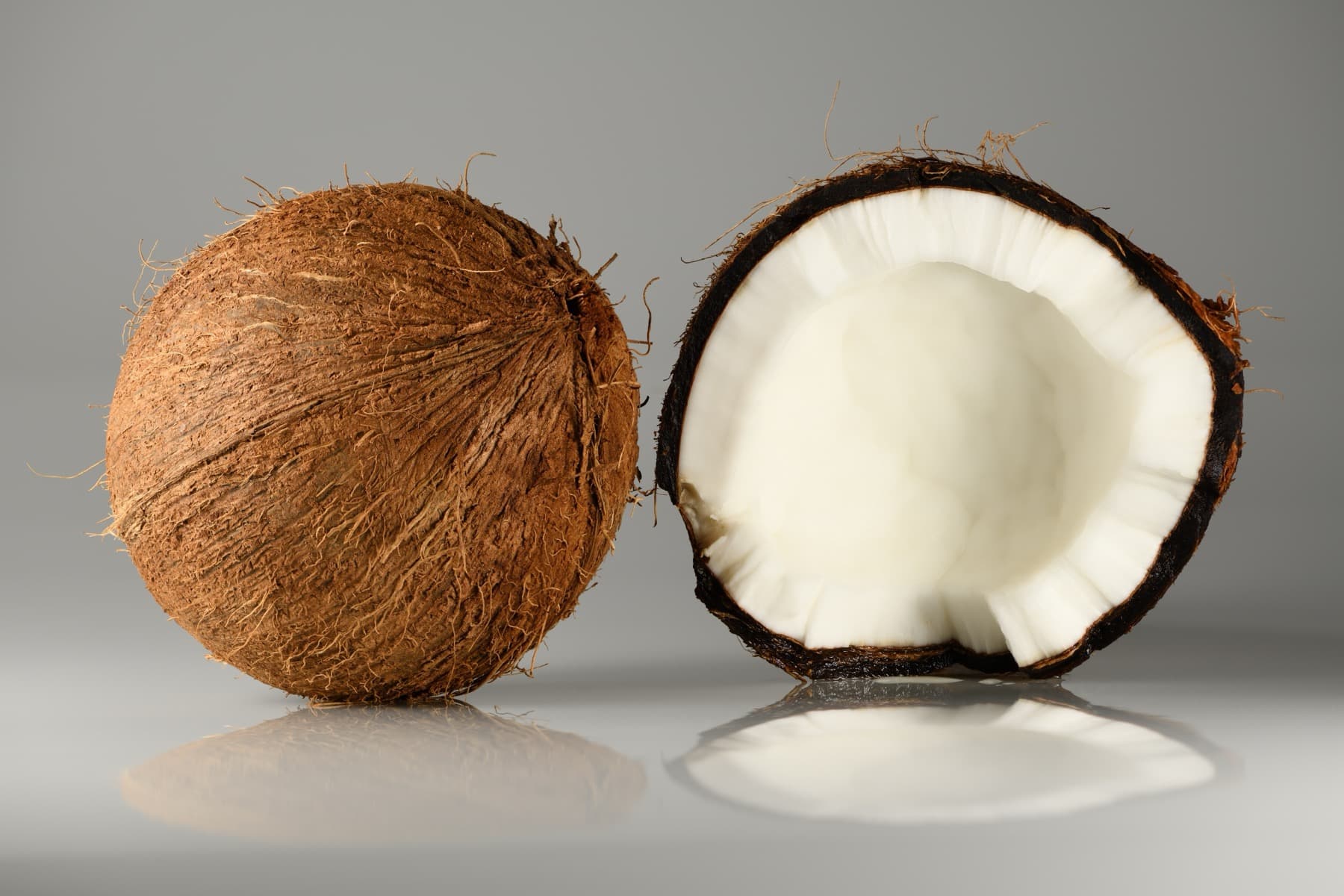 A whole coconut beside a coconut opened to show the white meat